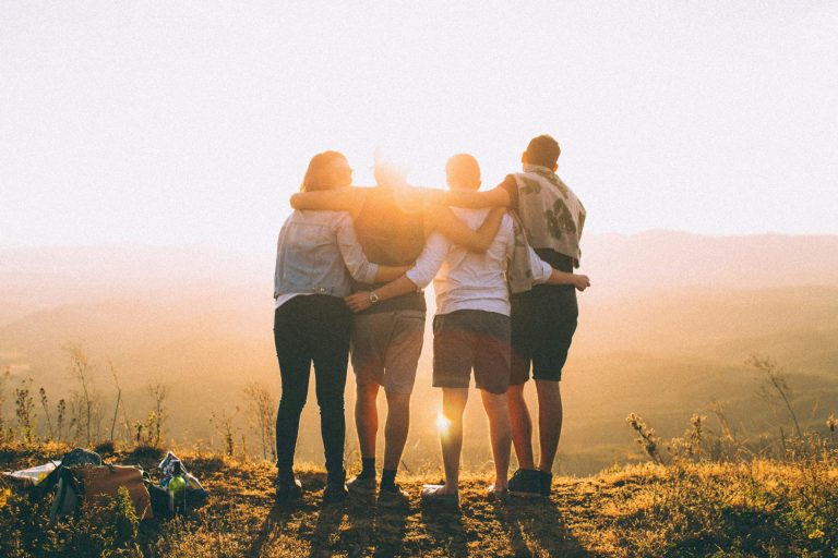 Group of people hugging together facing a sunset used on GesherEU's first impressions article